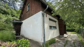 Einfaches Haus mit Holzverkleidung und weißem Putz, umgeben von viel Grün.