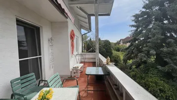 Gemütlicher Balkon mit roten Fliesen und Gartenmöbeln, ideal für entspannte Stunden im Freien mit Weitblick.