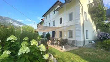 Geräumige Terrasse mit Sonnensegel und Gartenmöbeln, umgeben von grüner Natur und Bergblick.