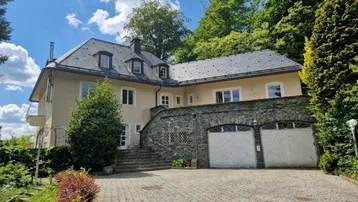 Repräsentative Villa mit Schieferdach und integrierter Doppelgarage, umgeben von üppigem Grün.