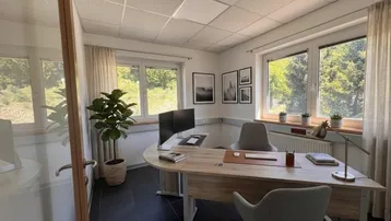 Modernes Büro mit ergonomischem Schreibtisch, zwei Monitoren und Blick ins Grüne durch große Fenster.