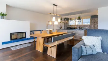 Offener Wohn-Essbereich mit Kamin, Holzboden und Blick auf die moderne Küche.