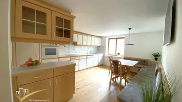 Helle Küche mit Holzboden, Einbauküche und gemütlicher Essecke am Fenster.