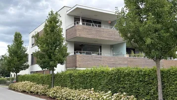 Modernes Mehrfamilienhaus mit Balkonen, umgeben von gepflegten Hecken und Bäumen.