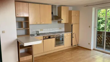 Helle Küchenzeile mit Holzfronten, integrierten Geräten und Zugang zum Balkon.