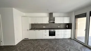 Moderne Einbauküche mit weißen Schränken, integriertem Backofen und Zugang zu einer Terrasse.
