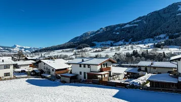 Winterlandschaft mit verschneiten Häusern und majestätischem Bergblick unter blauem Himmel.