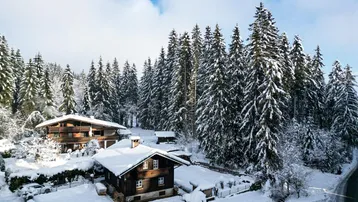 Winterliche Luftaufnahme eines Anwesens mit mehreren Häusern, umgeben von verschneiten Wäldern und Bergen.