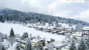 Panoramablick auf ein verschneites Bergdorf mit dichten Wäldern und einer malerischen Winterlandschaft.