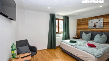 Gemütliches Schlafzimmer mit Holzwand, Doppelbett und Fernseher, ideal für entspannte Abende.