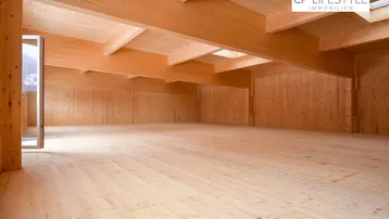Großer, leerer Innenraum mit sichtbaren Holzdeckenbalken und Holzwänden, bereit für den Ausbau.