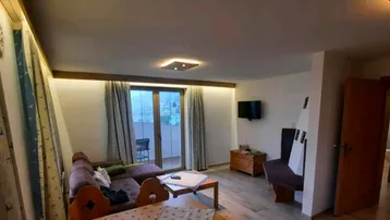 Gemütliches Wohnzimmer mit Sofa, Holzboden und Zugang zu einem Balkon oder einer Terrasse.