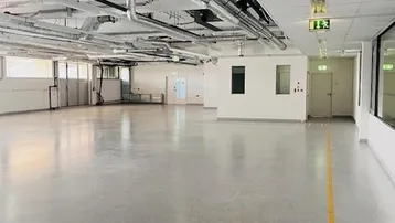 Großer, leerer Raum mit sichtbaren Lüftungsrohren an der Decke und einem polierten Betonboden, ideal für gewerbliche Nutzung.