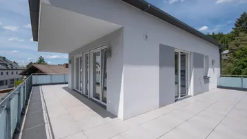 Große, helle Dachterrasse mit Fliesenboden und moderner Glasbrüstung, ideal für Entspannung.