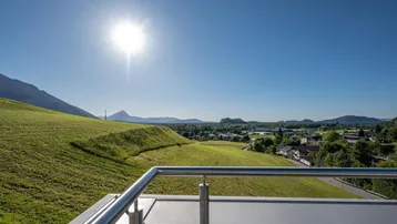 Sonniger Ausblick von der Terrasse auf die weite grüne Landschaft und die Berge.