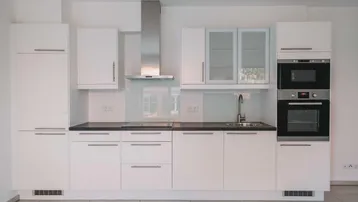 Helle, moderne Einbauküche in Weiß mit integrierten Geräten, Kochfeld und Dunstabzugshaube.