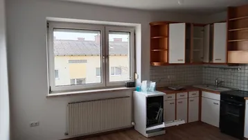 Küche mit Laminatboden, weißen und holzfarbenen Schränken, Spülmaschine und Fensterblick.
