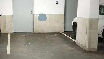 Tiefgaragenstellplatz mit Betonboden, weißen Wänden, grauen Türen und sichtbaren Installationen an der Decke.