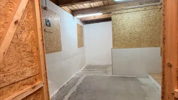 Innenraum mit OSB-Plattenwänden, Holzdecke und Betonboden, beleuchtet von Leuchtstoffröhren.
