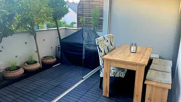 Gemütliche Terrasse mit Holztisch, Sitzbank und Grillbereich, umgeben von Topfpflanzen.