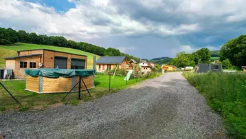 Blick auf eine ländliche Siedlung mit kleinen Häusern, Schotterweg und grünen Hügeln unter bewölktem Himmel.