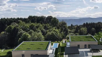 Luftaufnahme von modernen Häusern mit Gründächern, Pool und Bergblick in grüner Umgebung.