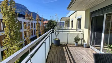 Geräumiger Balkon mit Holzboden, Pflanzen und einem schönen Blick auf die umliegenden Berge.