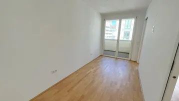 Leeres Zimmer mit Parkettboden und Zugang zu einem französischen Balkon.