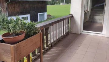 Gefliester Balkon mit Holzbalkongeländer und Blick auf grüne Wiesen und Berge.