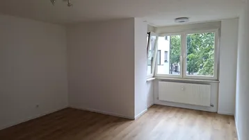 Heller, leerer Wohnraum mit Laminatboden und großen Fenstern, die viel Tageslicht hereinlassen.