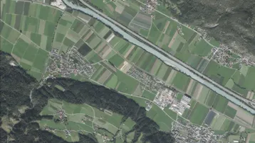 Luftaufnahme einer ländlichen Landschaft mit Feldern, einem Fluss, Wäldern und Bergen im Hintergrund.