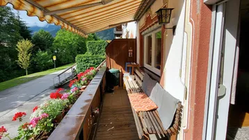 Sonniger Balkon mit gestreifter Markise, Holzboden und Blumenkästen mit Bergblick.