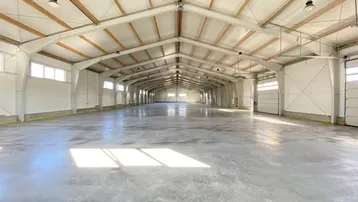 Geräumige, leere Lagerhalle mit hohen Decken, Betonboden und natürlichem Lichteinfall durch Fenster.