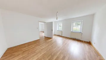 Helles, leeres Zimmer mit Laminatboden und zwei Fenstern, bereit zur individuellen Gestaltung.