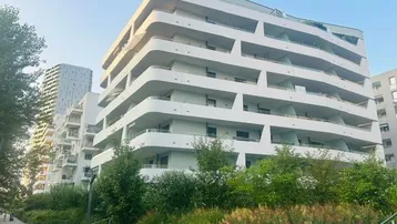 Modernes Wohngebäude mit geschwungenen Balkonen und begrünten Außenanlagen in urbaner Umgebung.