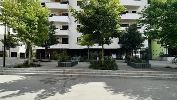 Modernes Wohngebäude mit weißer Fassade, zahlreichen Balkonen und grüner Umgebung unter blauem Himmel.