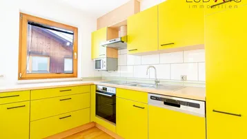 Moderne Küche mit leuchtend gelben Schränken, integrierten Geräten und Fenster.