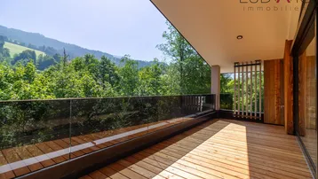 Geräumiger Balkon mit Holzboden, Glasgeländer und weitem Blick auf die umliegende Berglandschaft.
