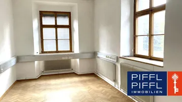 Heller Raum mit Fischgrätparkettboden, hohen Decken und großen Holzfenstern, ideal als Büro oder Wohnbereich.