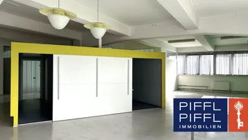 Großer, heller Büroraum mit hohen Decken, großen Fenstern und einer modernen Trennwand.