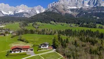 Luftaufnahme eines Baugrundstücks in ländlicher Umgebung mit Blick auf die Berge und umliegende Häuser.