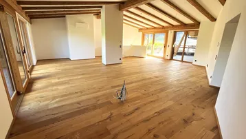 Geräumiger Wohnbereich mit Holzbalkendecke, Parkettboden und großen Fenstern für viel Tageslicht.