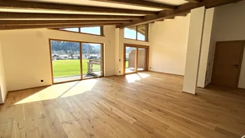 Lichtdurchfluteter Wohnbereich mit Holzboden, hohen Fenstern und weitem Blick ins Grüne.