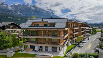 Modernes Mehrfamilienhaus in Holzbauweise mit Balkonen und Bergblick, umgeben von Grünflächen.