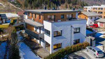 Moderne Wohnanlage mit Holz- und Putzfassade in alpiner Umgebung, umgeben von Bergen und Schnee.