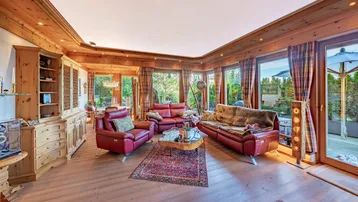 Gemütliches Wohnzimmer mit viel Holz, roten Ledersofas und großen Fenstern, die viel Licht hereinlassen.