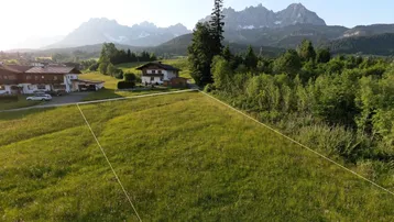 Luftaufnahme eines grünen Grundstücks mit Bergblick und angrenzenden Häusern in ländlicher Umgebung.