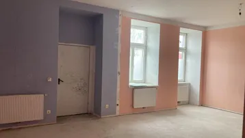 Geräumiger Innenraum in Renovierung mit teilweise gestrichenen Wänden und Heizkörpern unter den Fenstern.