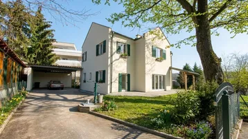 Vorderansicht des Hauses mit gepflegtem Vorgarten, Carport und Zufahrt an einem sonnigen Tag.
