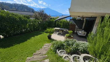 Gepflegter Gartenbereich mit sonniger Terrasse, Sitzgelegenheiten und Blick auf die umliegende Berglandschaft.